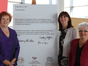 Three women with written statement expressing the commitment of The National Assembly for Wales, Welsh Ministers and Welsh Local Government to increasing the number of women in public office in Wales